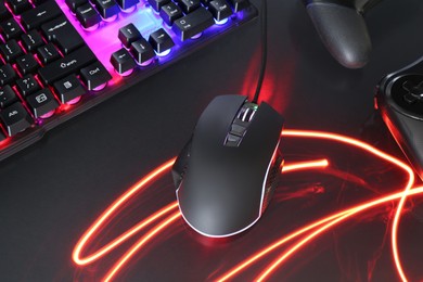 Photo of Computer mouse, RGB keyboard and game controllers in neon lights on dark background, closeup