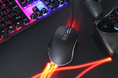 Computer mouse, RGB keyboard and game controllers in neon lights on dark background, closeup