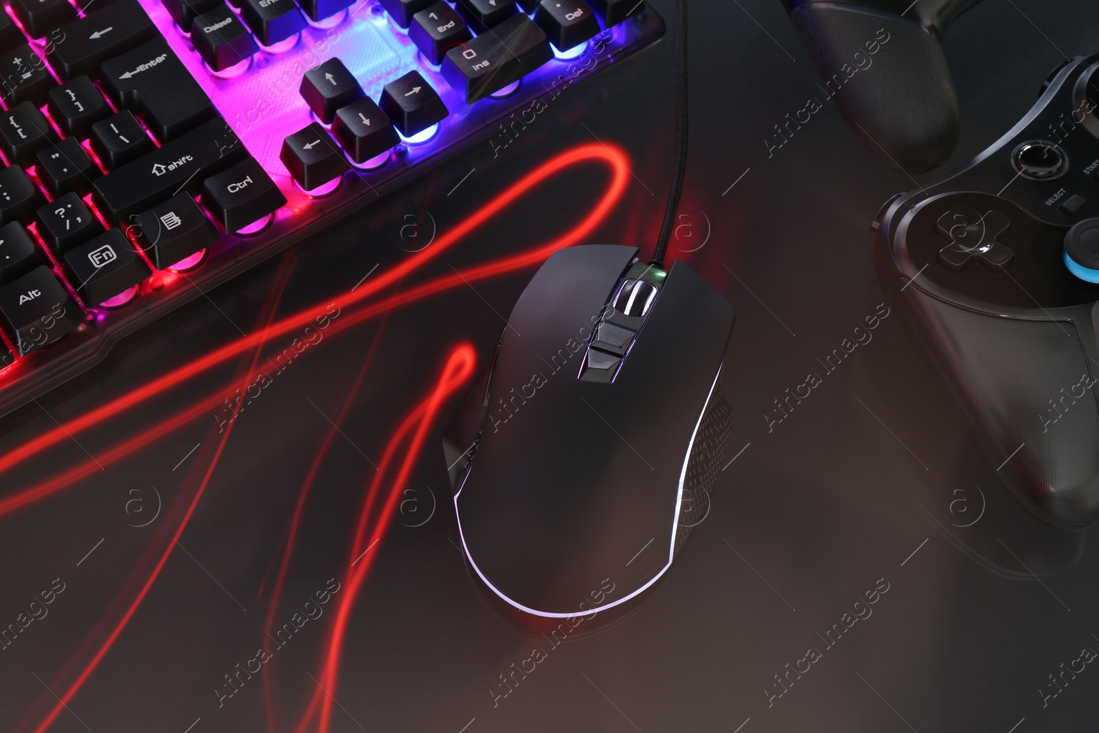 Photo of Computer mouse, RGB keyboard and game controllers in neon lights on dark background, closeup