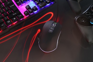 Photo of Computer mouse, RGB keyboard and game controllers in neon lights on dark background, closeup