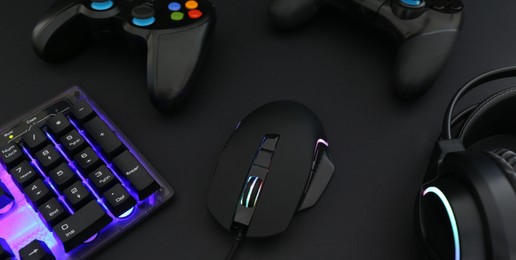 Photo of Computer mouse, headset, RGB keyboard and game controllers on black background, closeup