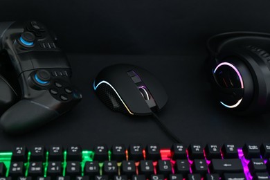 Photo of Computer mouse, headset, RGB keyboard and game controller on black background, closeup