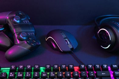 Photo of Computer mouse, headset, RGB keyboard and game controllers in neon lights on dark background, closeup