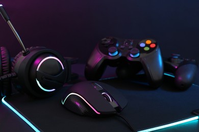 Photo of Computer mouse, headset and game controllers in neon lights on dark background, closeup