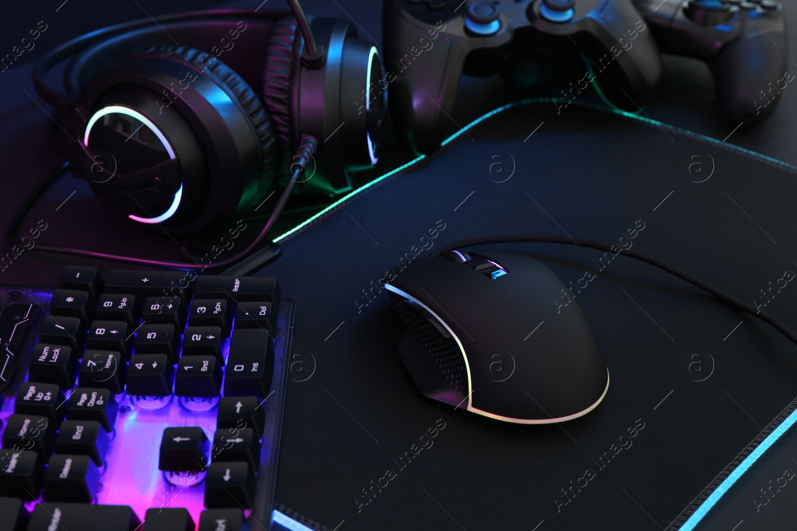 Photo of Computer mouse, RGB keyboard, headset and game controllers on dark background, closeup