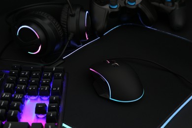 Photo of Computer mouse, RGB keyboard, headset and game controller on dark background, closeup