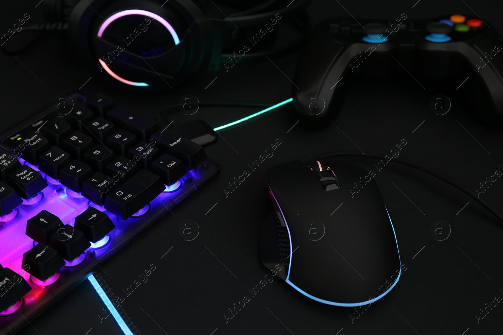 Photo of Computer mouse, RGB keyboard, headset and game controller on dark background, closeup