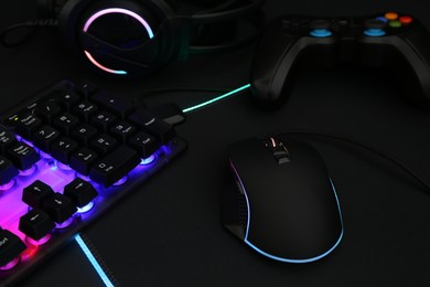 Computer mouse, RGB keyboard, headset and game controller on dark background, closeup