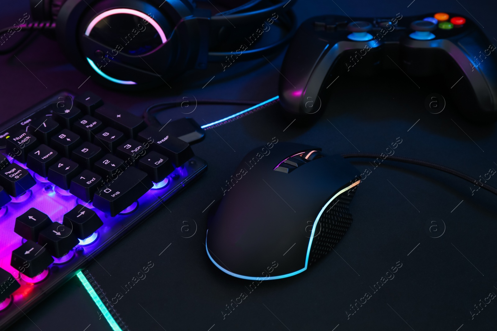 Photo of Computer mouse, RGB keyboard, headset and game controller on dark background, closeup