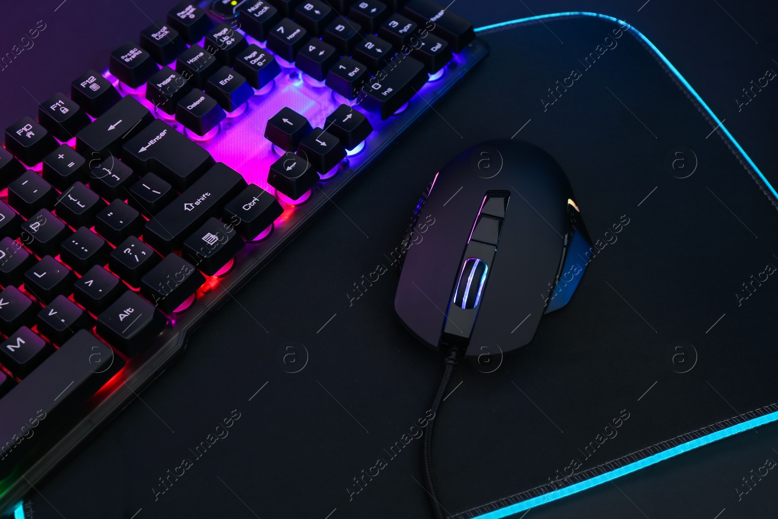 Photo of Computer mouse, mousepad and RGB keyboard on dark background, closeup