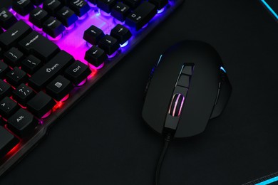 Computer mouse, mousepad and RGB keyboard on dark background, closeup