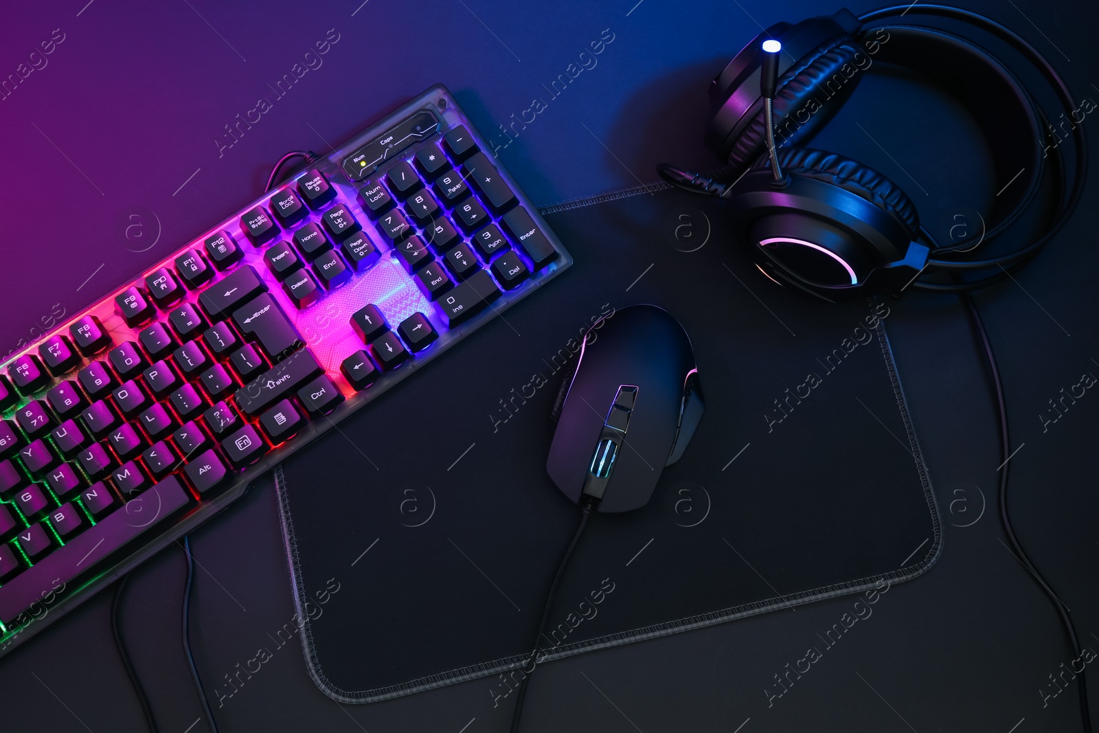 Photo of Computer mouse, headset and RGB keyboard in neon lights on dark background, flat lay