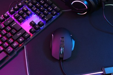 Photo of Computer mouse, headset and RGB keyboard in neon lights on dark background, above view