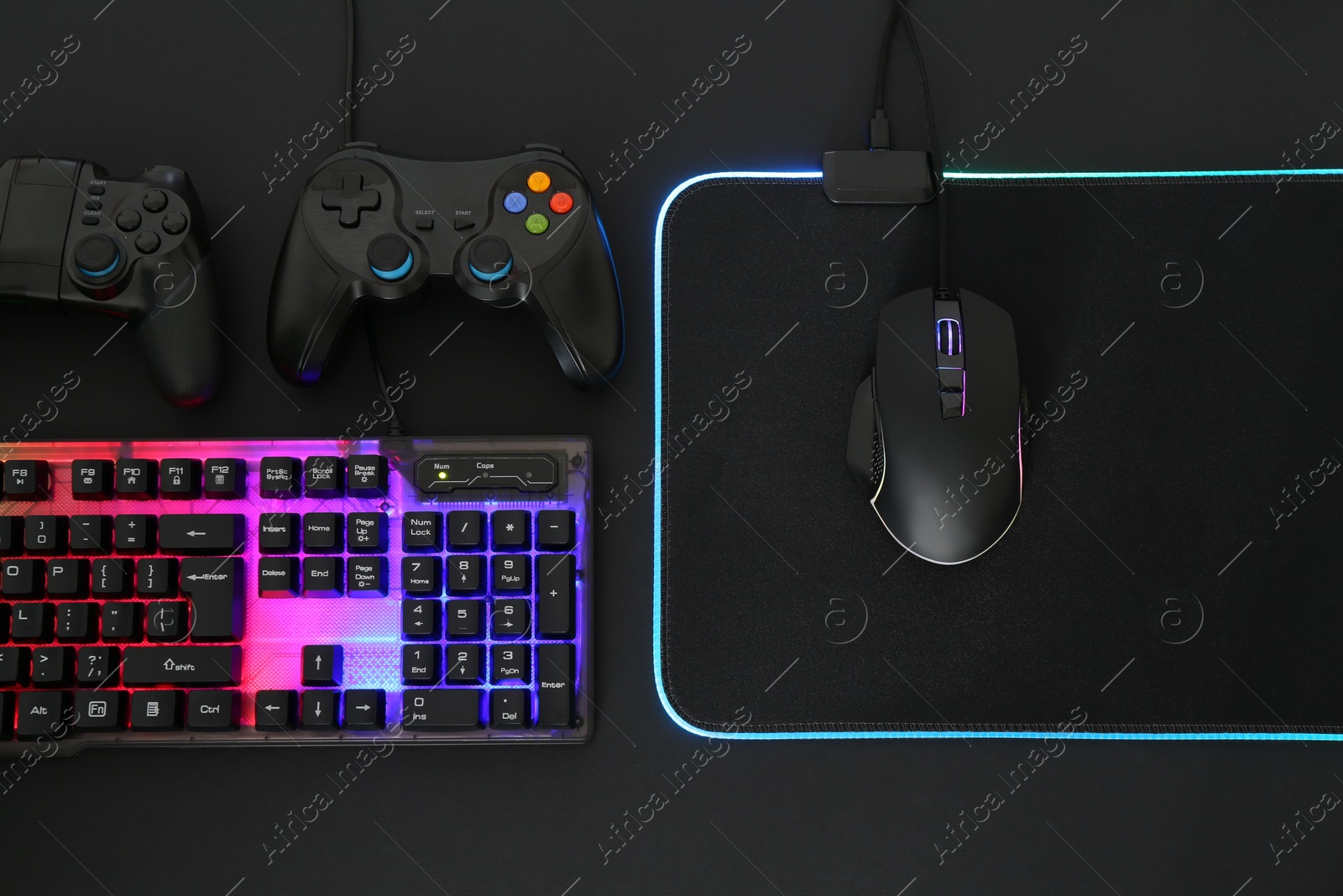 Photo of Computer mouse, RGB keyboard and game controllers on black background, flat lay