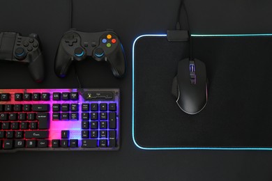 Photo of Computer mouse, RGB keyboard and game controllers on black background, flat lay