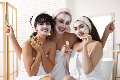 Happy friends with facial masks and cucumber slices in bathroom. Spa party