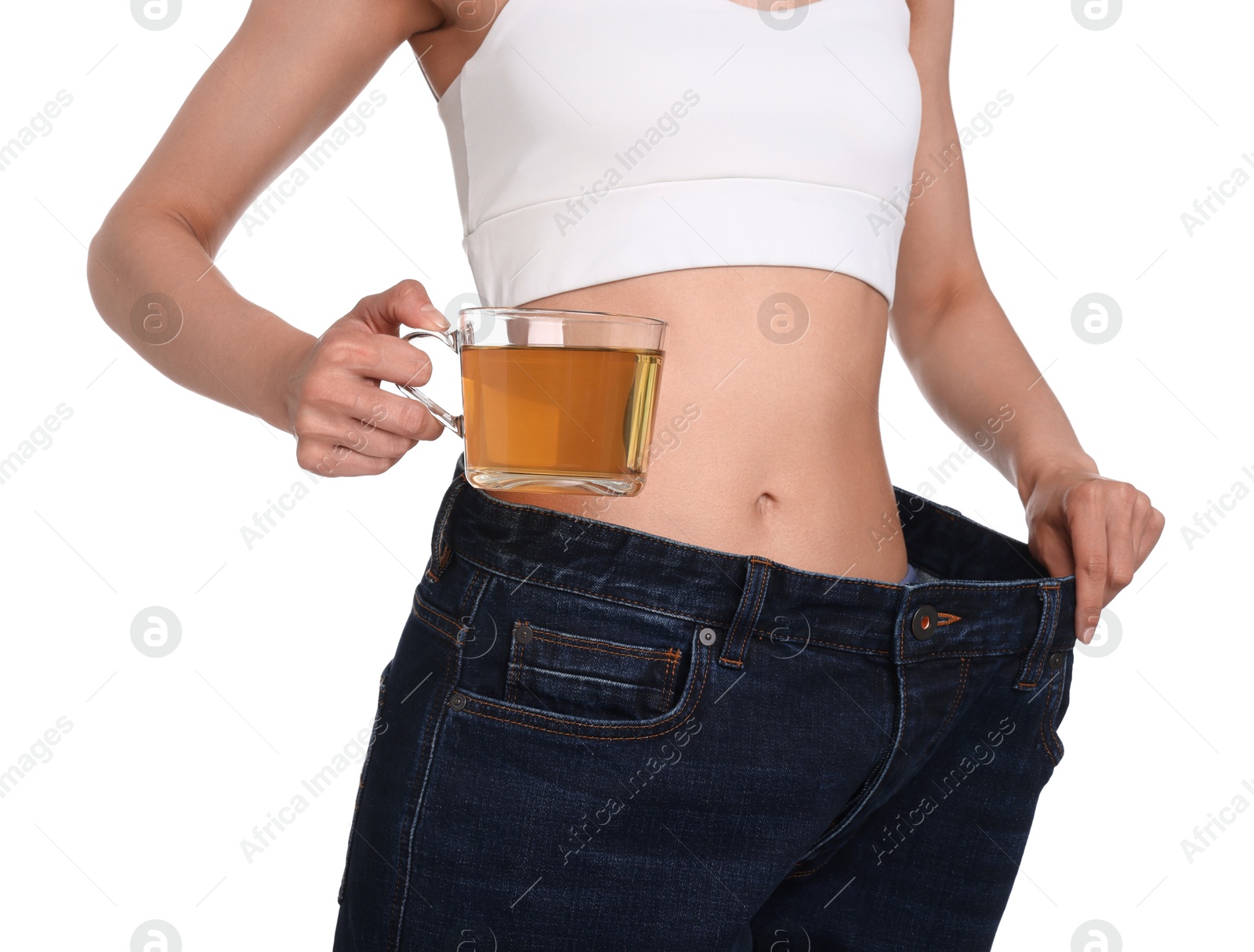 Photo of Weight loss concept. Woman with cup of diet tea and big pants on white background, closeup