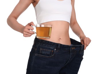 Photo of Weight loss concept. Woman with cup of diet tea and big pants on white background, closeup