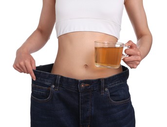 Photo of Weight loss concept. Woman with cup of diet tea and big pants on white background, closeup