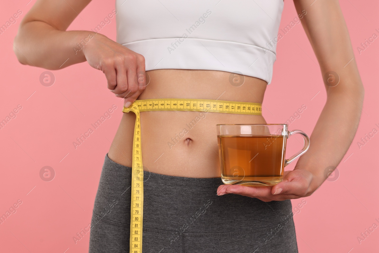 Photo of Weight loss concept. Woman with cup of diet tea and measuring tape on pink background, closeup