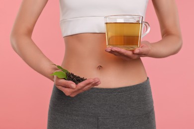 Photo of Weight loss concept. Woman with cup of diet tea and dry leaves on pink background, closeup