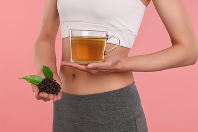 Weight loss concept. Woman with cup of diet tea and dry leaves on pink background, closeup