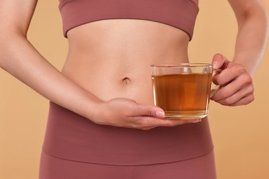 Photo of Weight loss concept. Woman with cup of diet tea on beige background, closeup