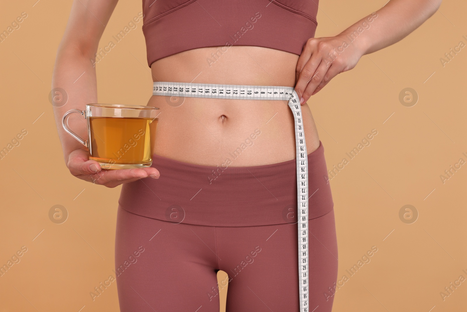 Photo of Weight loss concept. Woman with cup of diet tea and measuring tape on beige background, closeup