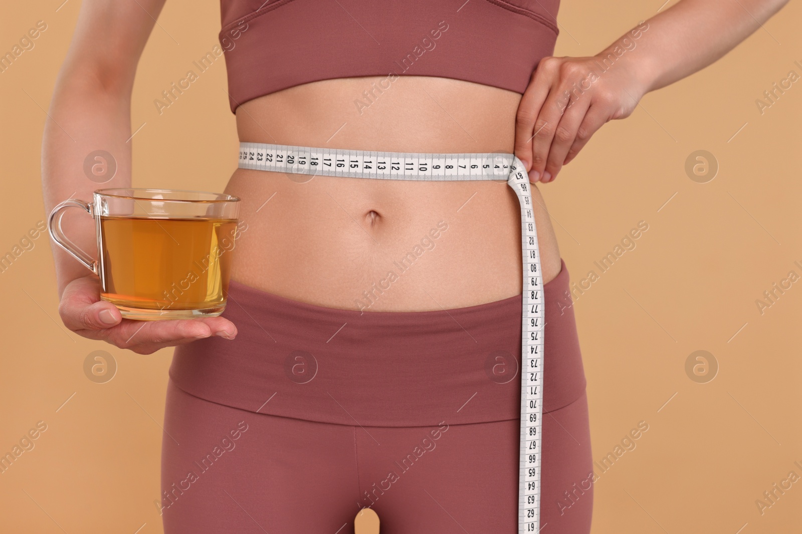 Photo of Weight loss concept. Woman with cup of diet tea and measuring tape on beige background, closeup