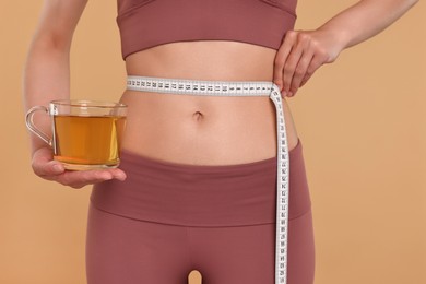 Weight loss concept. Woman with cup of diet tea and measuring tape on beige background, closeup