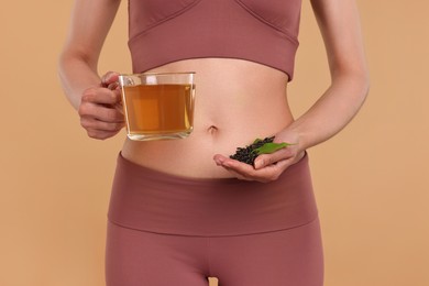 Photo of Weight loss concept. Woman with cup of diet tea and dry leaves on beige background, closeup