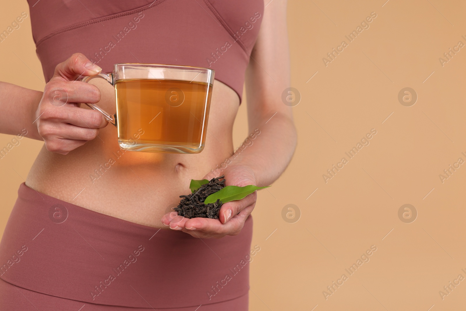 Photo of Weight loss concept. Woman with cup of diet tea and dry leaves on beige background, closeup