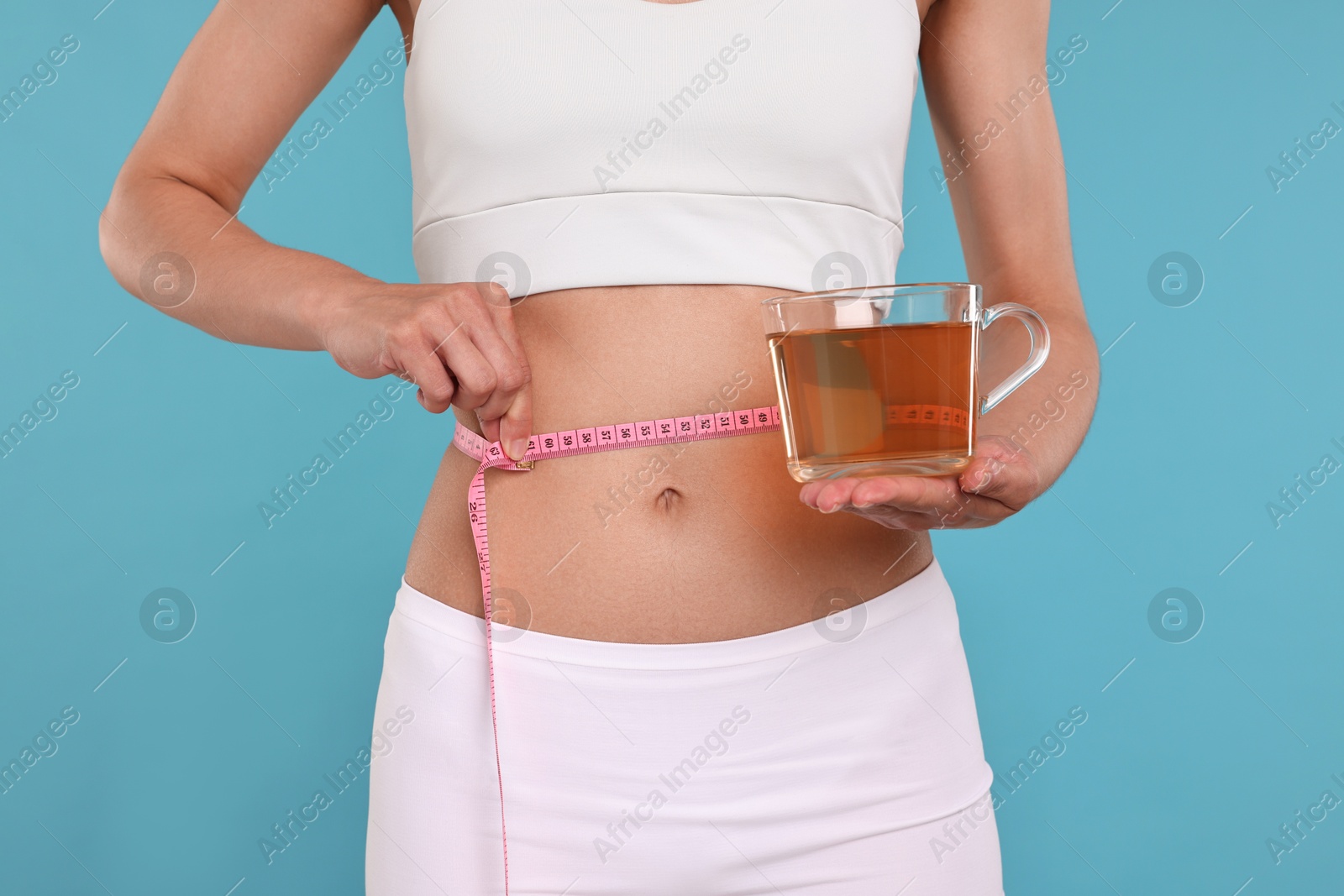 Photo of Weight loss concept. Woman with cup of diet tea and measuring tape on light blue background, closeup