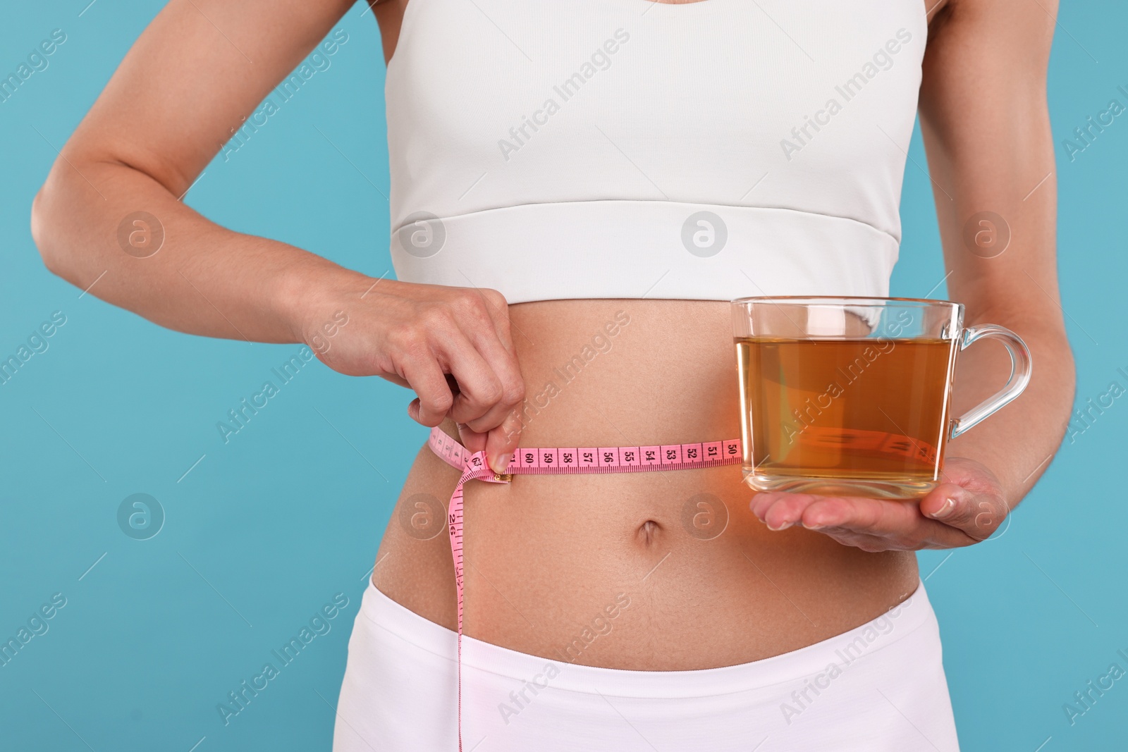 Photo of Weight loss concept. Woman with cup of diet tea and measuring tape on light blue background, closeup