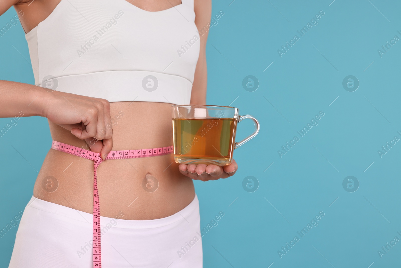 Photo of Weight loss concept. Woman with cup of diet tea and measuring tape on light blue background, closeup