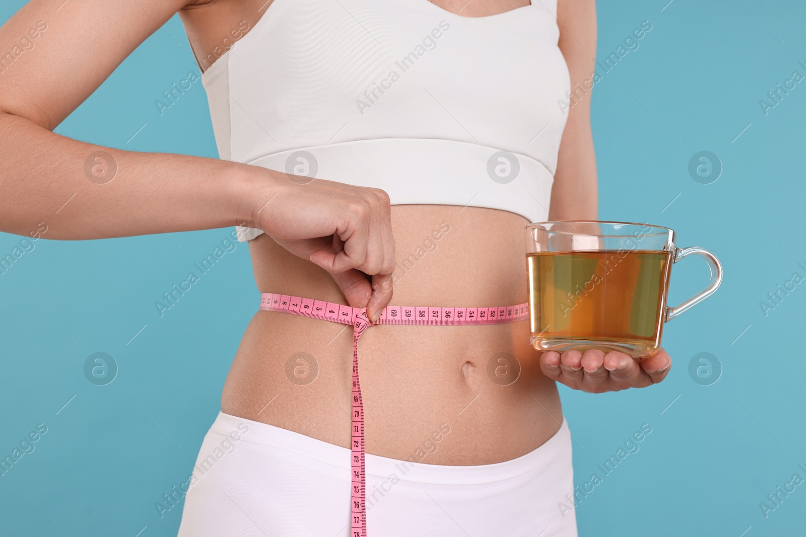 Photo of Weight loss concept. Woman with cup of diet tea and measuring tape on light blue background, closeup