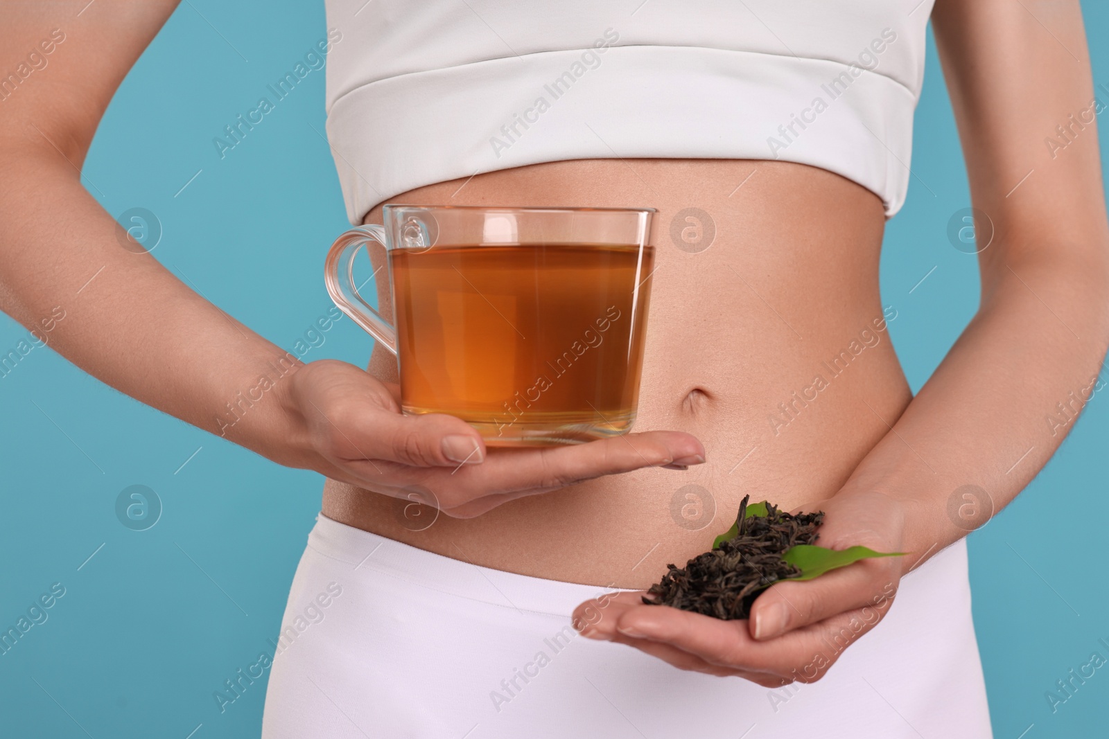 Photo of Weight loss concept. Woman with cup of diet tea and dry leaves on light blue background, closeup