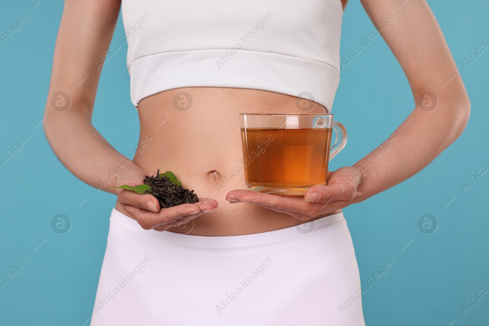 Photo of Weight loss concept. Woman with cup of diet tea and dry leaves on light blue background, closeup