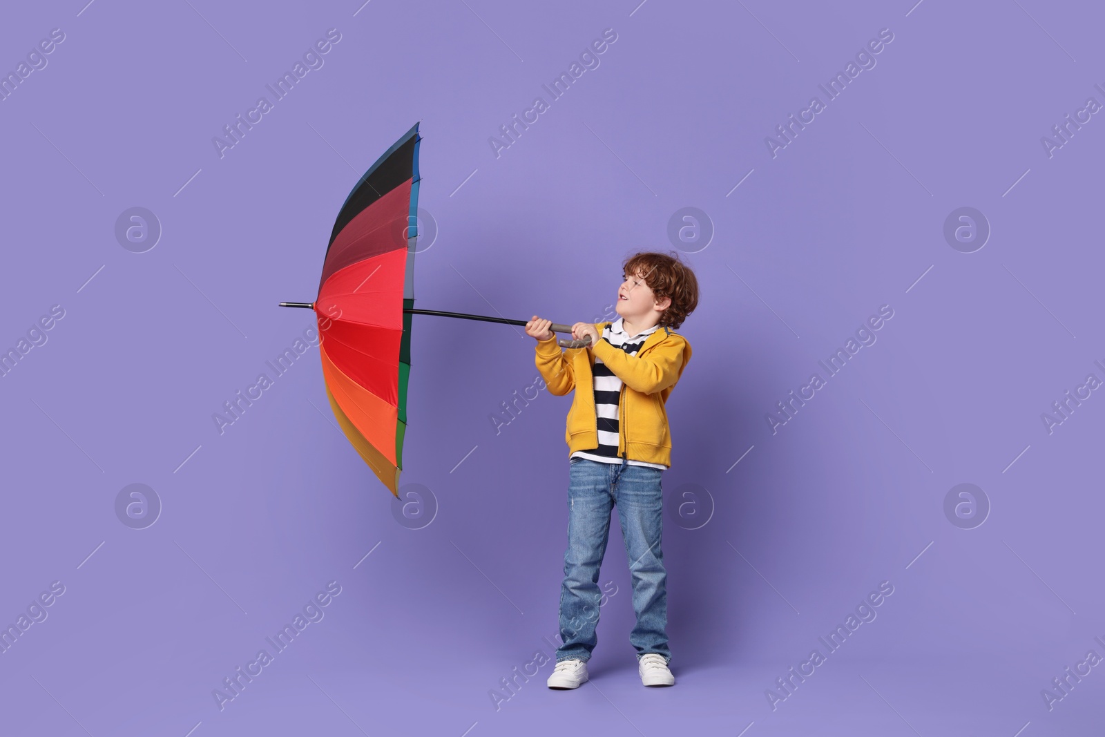 Photo of Little boy with rainbow umbrella on purple background