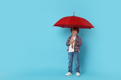 Photo of Little boy with red umbrella on light blue background, space for text