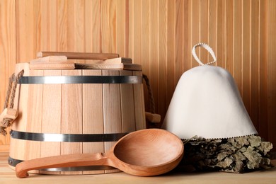 Photo of Oak sauna whisk, felt wool hat, bucket and ladle on wooden surface