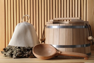 Oak sauna whisk, felt wool hat, bucket and ladle on wooden surface