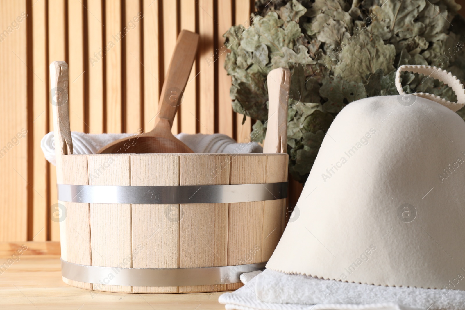 Photo of Sauna equipment. Felt wool hat, towels, oak whisk, bucket and ladle on wooden surface