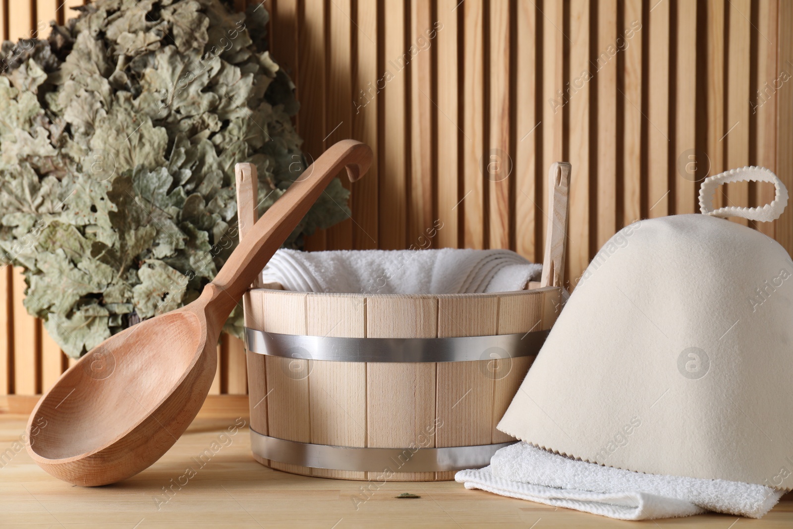 Photo of Oak sauna whisk, felt wool hat, towels, bucket and ladle on wooden surface