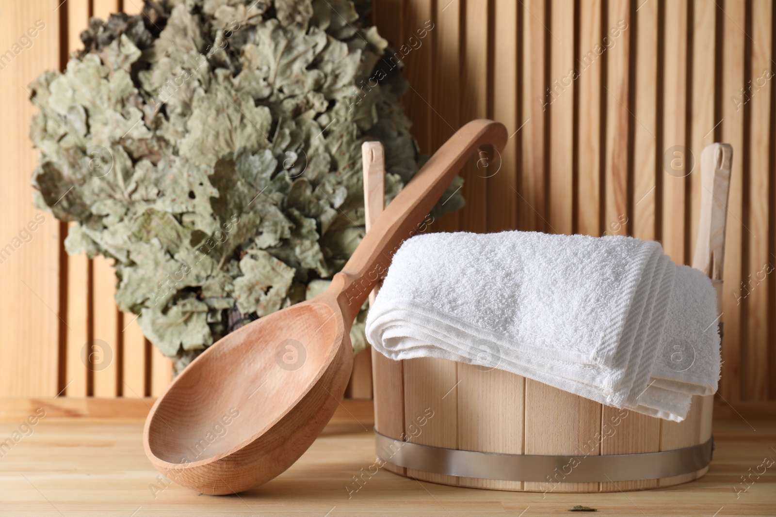 Photo of Sauna equipment. Bucket, ladle, towel and oak whisk on wooden surface