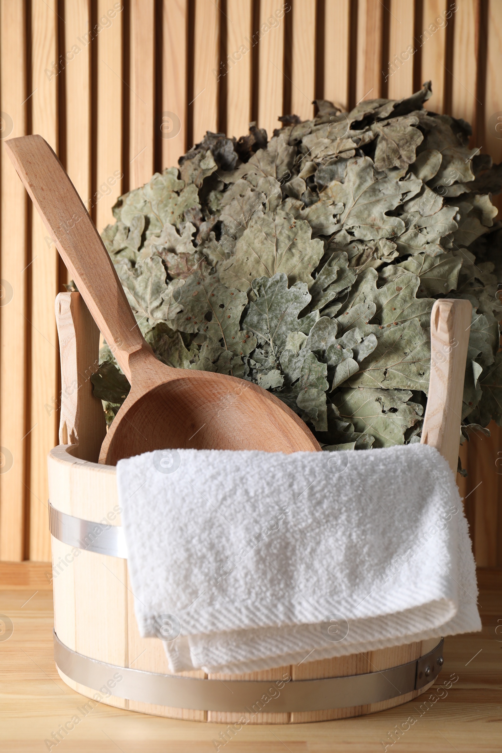 Photo of Sauna equipment. Bucket, ladle, towel and oak whisk on wooden surface