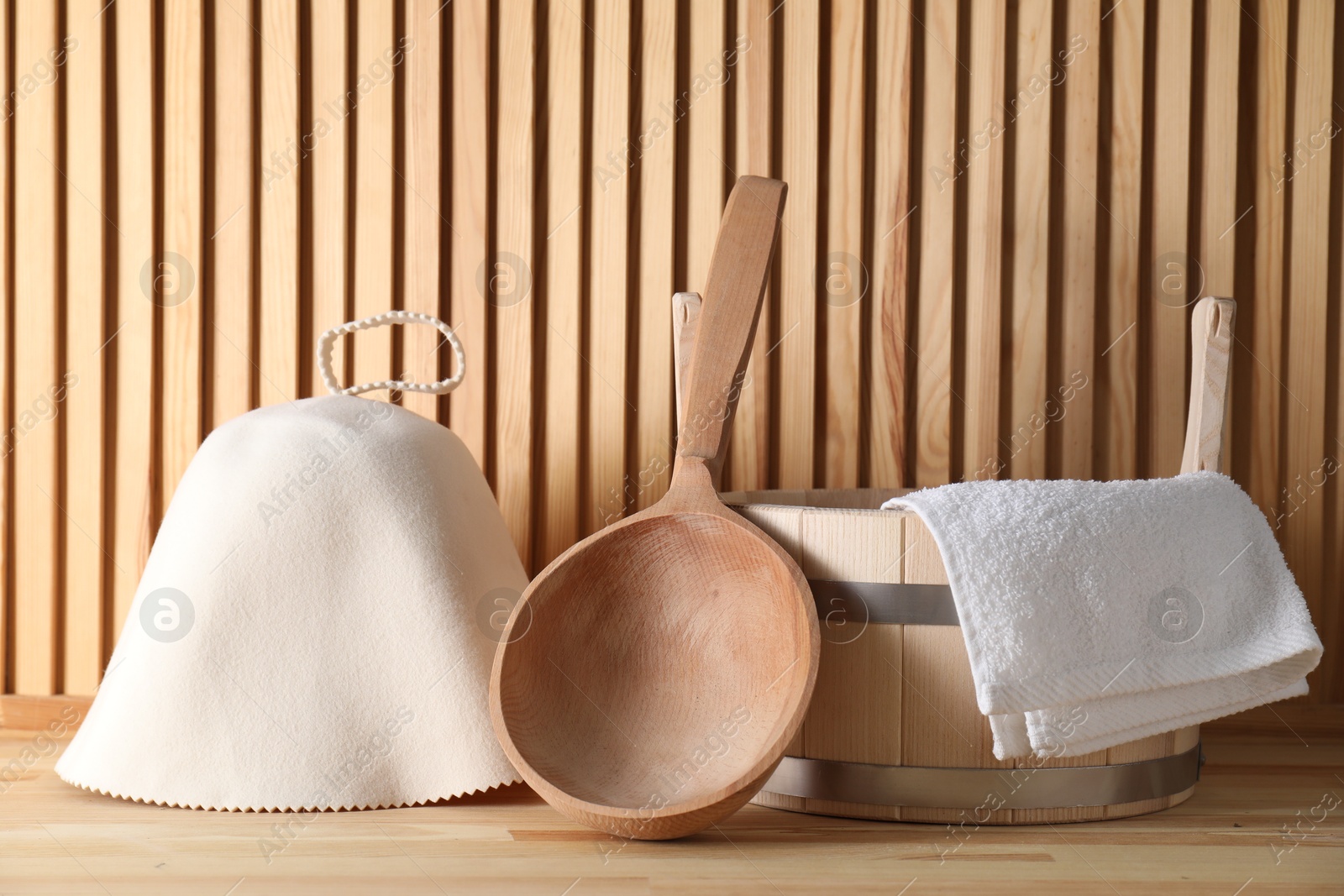 Photo of Sauna equipment. Felt wool hat, towel, bucket and ladle on wooden surface