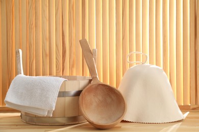 Photo of Sauna equipment. Felt wool hat, towel, bucket and ladle on wooden surface