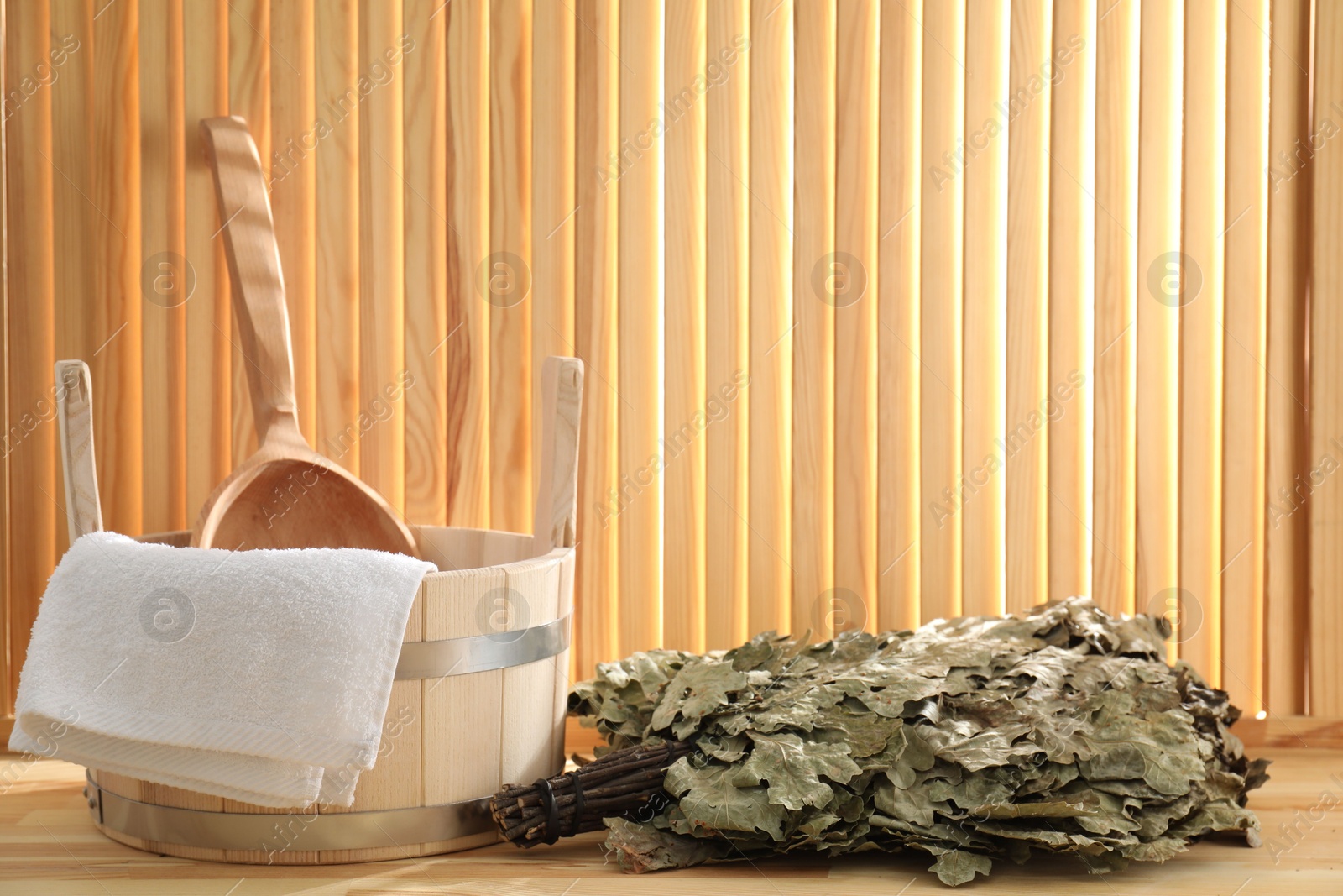 Photo of Sauna equipment. Bucket, ladle, towel and oak whisk on wooden surface