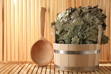 Oak sauna whisk in bucket and ladle on wooden surface